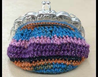 May include: A small crocheted coin purse with a silver clasp. The purse is made with a variety of colours, including blue, purple, pink, orange, and black.