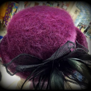May include: A purple fuzzy hat with a black mesh bow and feather accent.