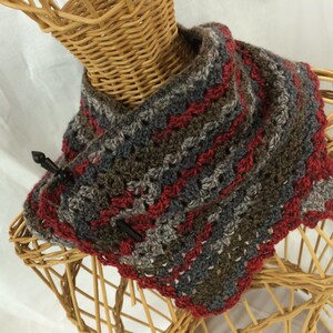 Puede incluir: Una capucha de ganchillo en tonos grises, marrones y rojos. La capucha está hecha con un punto texturizado y tiene un borde festoneado.