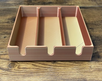 May include: A three-compartment organizer in a light peach color. The rectangular tray has rounded cutouts on the front edge and is designed to hold items. The interior compartments are a light beige color.