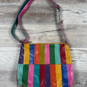 May include: A multi-colored crossbody bag featuring vertical panels in shades of yellow, blue, orange, green, pink, purple, and red. The bag has a long, adjustable shoulder strap with a pink exterior and a teal interior, and a top zipper closure.