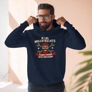 Op de afbeelding: Marineblauwe hoodie met de tekst "REAL MILLWRIGHTS" boven een schedelafbeelding met gekruiste moersleutels en de zin "TURN CHAOS INTO PRECISION" op een rode banner. De hoodie heeft een capuchon met trekkoord en lange mouwen.