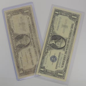 May include: Two vintage US one dollar bills in protective plastic sleeves. The bills are both from the same series, with the serial number C13561966A printed on both. The bills are in good condition, with some wear and tear.