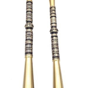 May include: Two antique brass door handles with ornate detailing. The handles have a conical shape with decorative bands and floral patterns. The mounting plates are also detailed. The handles are displayed against a white background.