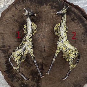 May include: Two black and yellow giraffe-shaped metal hooks. The hooks are mounted on a wooden surface. The hooks are numbered 1 and 2.