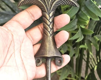 Puede incluir: Un gancho de árbol de palma de color bronce. El gancho presenta un diseño detallado de hojas de palma en la parte superior, un tronco trenzado y una base acampanada con orificios de montaje. El gancho está diseñado para colgar objetos y añade un toque decorativo.