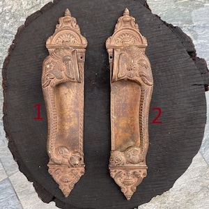 Puede incluir: Dos tiradores de puerta de latón antiguo con intrincados diseños de cabeza de elefante. Los tiradores son ornamentados y presentan tallas detalladas.