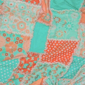 May include: A patchwork quilt featuring a mix of floral and dotted patterns in shades of coral, mint green, and white. The quilt has a ruffled edge and a textured appearance, with a variety of floral and butterfly designs.