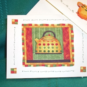 May include: A white card with a colorful illustration of a yellow teapot with red and green accents. The teapot is surrounded by a decorative border with red, green, and yellow stripes. The card has a white background with a decorative border.