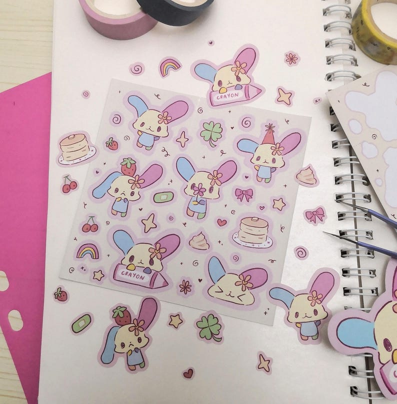 May include: A sheet of stickers featuring cute cartoon bunnies with pastel pink, blue, and yellow colors. The stickers include various designs, such as bunnies holding flowers, hearts, and a crayon. The sheet also includes other designs like stars, rainbows, and clover leaves.