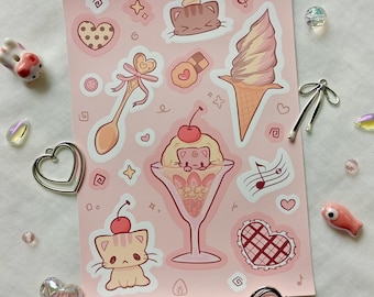 May include: A pink sticker sheet featuring kawaii-style illustrations of desserts and cats. The sheet includes images of ice cream cones, parfaits, cookies, spoons, musical notes, and hearts. Decorative charms and beads surround the sticker sheet.