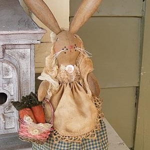 May include: A handmade fabric bunny doll wearing a brown dress with a blue and white gingham skirt and a lace trim. The bunny is holding a basket of carrots.