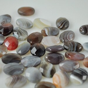 May include: A collection of smooth, oval-shaped agate stones in various shades of gray, brown, and white with intricate banding patterns.