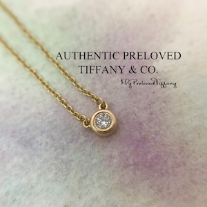 Puede incluir: Un collar de cadena de oro con un pequeño colgante redondo con un solo diamante. El colgante está engastado en un engaste de bisel. El collar está sobre un fondo blanco con el texto "AUTHENTIC PRELOVED TIFFANY & CO." y "My Preloved Tiffany" escrito en cursiva.
