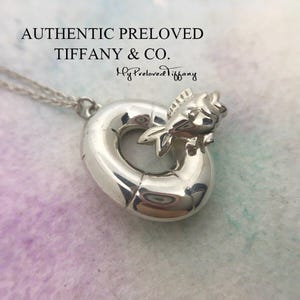Puede incluir: Un collar de plata con un dije de un pez nadando en un salvavidas. El dije es de Tiffany & Co. y dice "My Preloved Tiffany" en la parte posterior.