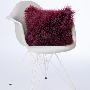 Op de afbeelding: Een bordeauxrood nep bont kussen op een witte stoel met een metalen frame.