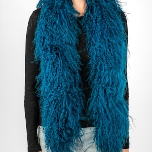 Peut inclure: Une écharpe en fausse fourrure bleu sarcelle avec de longues mèches hirsutes. L'écharpe est portée autour du cou d'une personne portant une chemise noire à manches longues et un jean bleu.