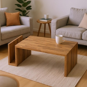 May include: A rectangular wooden coffee table with a natural light brown finish and a visible wood grain pattern. The table features a unique integrated vertical side compartment for storage and a flat top surface holding a single white ceramic mug.