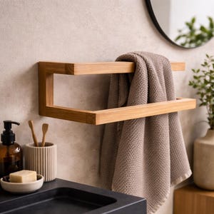 May include: A wooden towel rack mounted on a light-colored wall. The rack has a rectangular design and holds a folded beige towel. Other bathroom accessories include a soap dish, toothbrush holder, and a soap dispenser.
