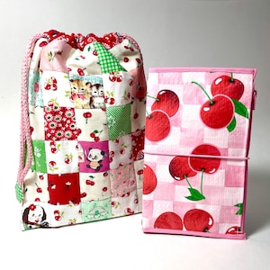 May include: A patchwork drawstring bag and a journal. The bag features a variety of fabrics with cherry and animal prints. The journal has a pink and white checkered pattern with large red cherry illustrations.