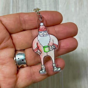 Puede incluir: Un Papá Noel rosa y blanco con un gorro rojo y sosteniendo una taza verde. Papá Noel lleva un mono rosa con ribete blanco y tiene barba blanca. Papá Noel es un llavero.