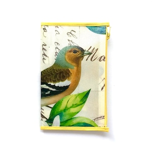Pode incluir: Uma bolsa retangular com zíper com um desenho de pássaro e flores. A bolsa apresenta um pássaro colorido com penas marrons, laranja e azuis e folhas verdes. O fundo tem escrita de roteiro e uma borda amarela.