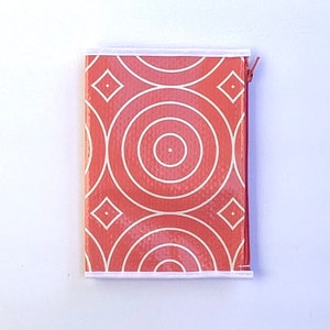 May include: A coral-colored zippered pouch with a white trim and a geometric pattern of concentric circles and diamonds.