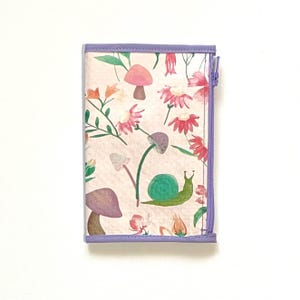 May include: A small, rectangular wallet with a floral and mushroom pattern. The design features pink flowers, purple mushrooms, and a green snail on a light pink background. The wallet has a purple zipper and trim.
