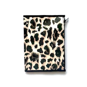 Puede incluir: Una pequeña bolsa negra con cremallera con un diseño de estampado de leopardo. La bolsa está hecha de un material suave y de tela.