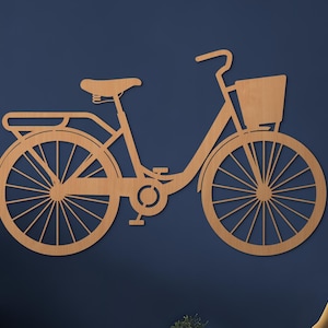 Può includere: Una sagoma da parete in legno color marrone chiaro a forma di bicicletta. Il design presenta un cestino anteriore, un portapacchi posteriore, una sella, un manubrio, pedali e due grandi ruote a raggi. La silhouette della bici è semplice.