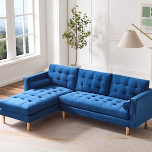 May include: A blue velvet sectional sofa with a tufted design and wooden legs. The sofa has a chaise lounge on the left side and a matching ottoman.