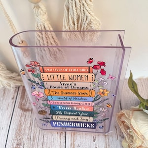 May include: A clear acrylic book stand with a stack of colorful books printed with titles like "Little Women", "Anne's House of Dreams", and "The Summer Book".