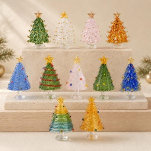 Puede incluir: Una colección de once árboles de Navidad de cristal en miniatura de varios colores, incluyendo verde, transparente, rosa, ámbar, azul y diseños multicolores. Cada árbol tiene una estrella dorada en la punta y una base de cristal sobre bloques.