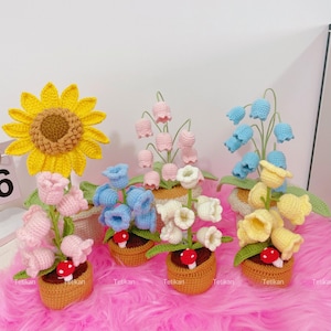 May include: A collection of handmade crochet flowers in small woven baskets. The flowers include a large yellow sunflower, pink, blue, white, and yellow bell-shaped flowers, and a small red mushroom. The word "Tetikan" is visible on the baskets.