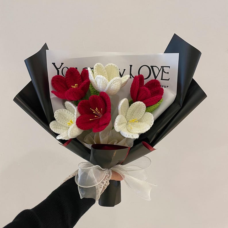 Pu&ograve; includere: Un mazzo di fiori all'uncinetto in rosso e bianco, avvolto in carta nera con un nastro bianco. La carta ha il testo "You My LOVE" stampato.