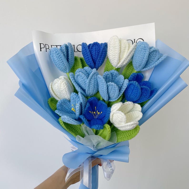 This is a blue-themed crochet bouquet with a total of 11 stems of flowers, including 3 dark blue tulips, 5 blue tulips, and 3 white tulips. Their leaves and stems are green, and they are wrapped with blue wrapping paper and ribbons.
