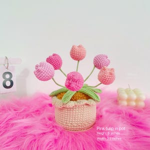 May include: A crocheted pink tulip arrangement in a pot. The pot is beige with a scalloped edge, and the tulips are various shades of pink. The arrangement is 6 inches tall and 3.5 inches wide. The text reads "Pink tulip in pot".