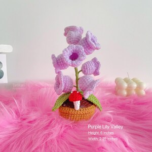 1 crochet purple lily of the valley potted plant lamp is placed on a pink blanket, the petals are purple, the leaves are green, and the crochet pot is brown; The size of the crochet potted plant lamp is approximately height: 6 inches, width: 2.25 inches