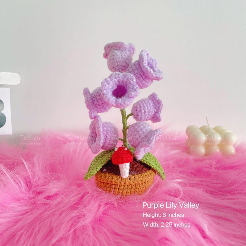 1 crochet purple lily of the valley potted plant lamp is placed on a pink blanket, the petals are purple, the leaves are green, and the crochet pot is brown; The size of the crochet potted plant lamp is approximately height: 6 inches, width: 2.25 inches