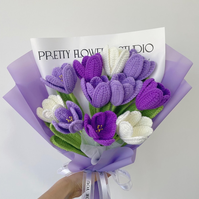 This is a purple-themed crochet bouquet with a total of 11 stems of flowers, including 3 dark purple tulips, 5 purple tulips, and 3 white tulips. Their leaves and stems are green, and they are wrapped with purple wrapping paper and ribbons.