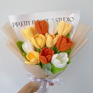 This is an orange-themed crochet bouquet with a total of 11 stems of flowers, including 3 orange tulips, 5 yellow tulips, and 3 white tulips. Their leaves and stems are green, and they are wrapped in champagne-colored wrapping paper and ribbons.