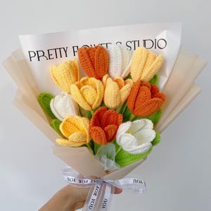 Pu&ograve; includere: Un mazzo di tulipani all'uncinetto in tonalit&agrave; arancio, giallo e bianco, avvolto in carta marrone con un nastro bianco che dice "Just for you".
