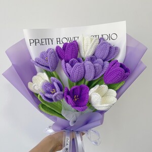 Pu&ograve; includere: Un mazzo di crochi all'uncinetto viola e bianchi avvolti in carta velina lavanda con un nastro bianco che dice "Per te". Il mazzo &egrave; etichettato "Pretty Flower Studio".