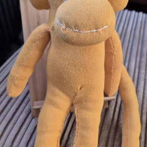May include: A yellow sock monkey doll with button eyes and stitched features. The monkey has a stitched smile and is standing upright. The doll is made from soft fabric and has a classic, whimsical design.