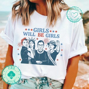 Pode incluir: T-shirt branca com a frase "GIRLS WILL BE GIRLS" acima de um gráfico de quatro mulheres. O gráfico inclui ilustrações de mulheres, estrelas e fogos de artifício em vermelho, branco e azul. A camisa tem gola redonda e mangas curtas.