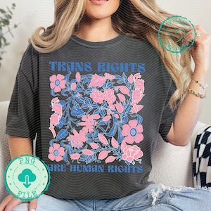 Könnte beinhalten: Dunkelgraues T-Shirt mit dem blauen Text "TRANS RIGHTS ARE HUMAN RIGHTS". Das Shirt hat ein florales Design in Rosa und Blau. Das Design ist mittig auf der Vorderseite des Shirts.