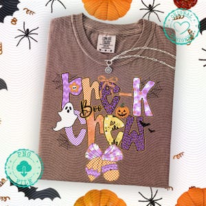 May include: Brown t-shirt with the text "Trick Boo Crew" in purple, orange, and yellow, featuring Halloween-themed graphics like a ghost, pumpkin, and bats. The shirt has a Comfort Colors tag and a silver necklace.