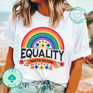 Pode incluir: Uma camiseta branca com um arco-íris, flores e o texto "Igualdade não machuca ninguém".