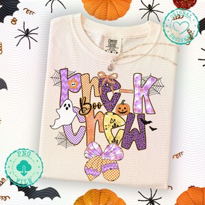 May include: Cream-colored sweatshirt with the words "Trick Boo Crew" in purple, orange, and yellow, featuring Halloween-themed graphics like a ghost, pumpkin, and spiderwebs. A bow graphic is at the bottom.