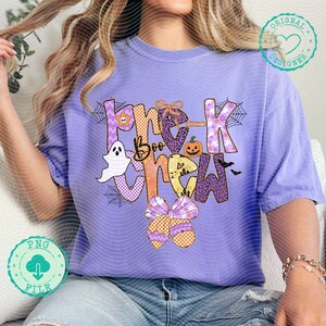 May include: A light purple t-shirt with the words "Boo Crew" in a Halloween-themed design. The design includes a ghost, pumpkin, spiderwebs, and bows. The shirt is a relaxed fit.